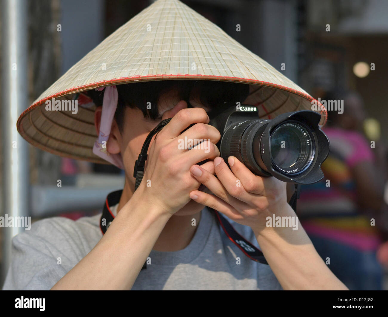 Giovane vietnamita street fotografo indossa un asiatico cappello conico e scatta una fotografia con la sua Canon fotocamera reflex digitale. Foto Stock