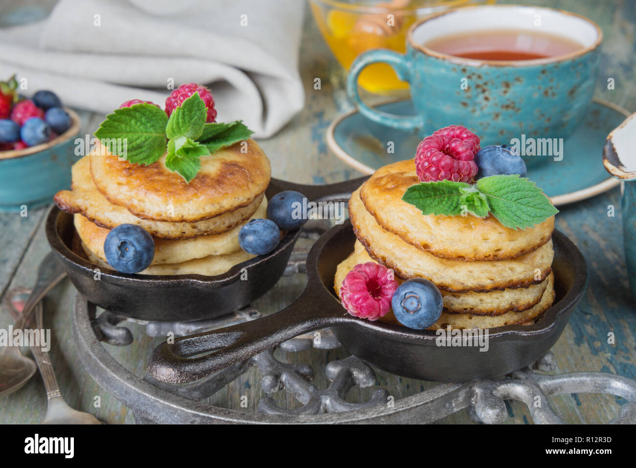 Colazione a base di frittelle in ghisa padelle, frutti di bosco freschi e il tè nero in stile rustico Foto Stock