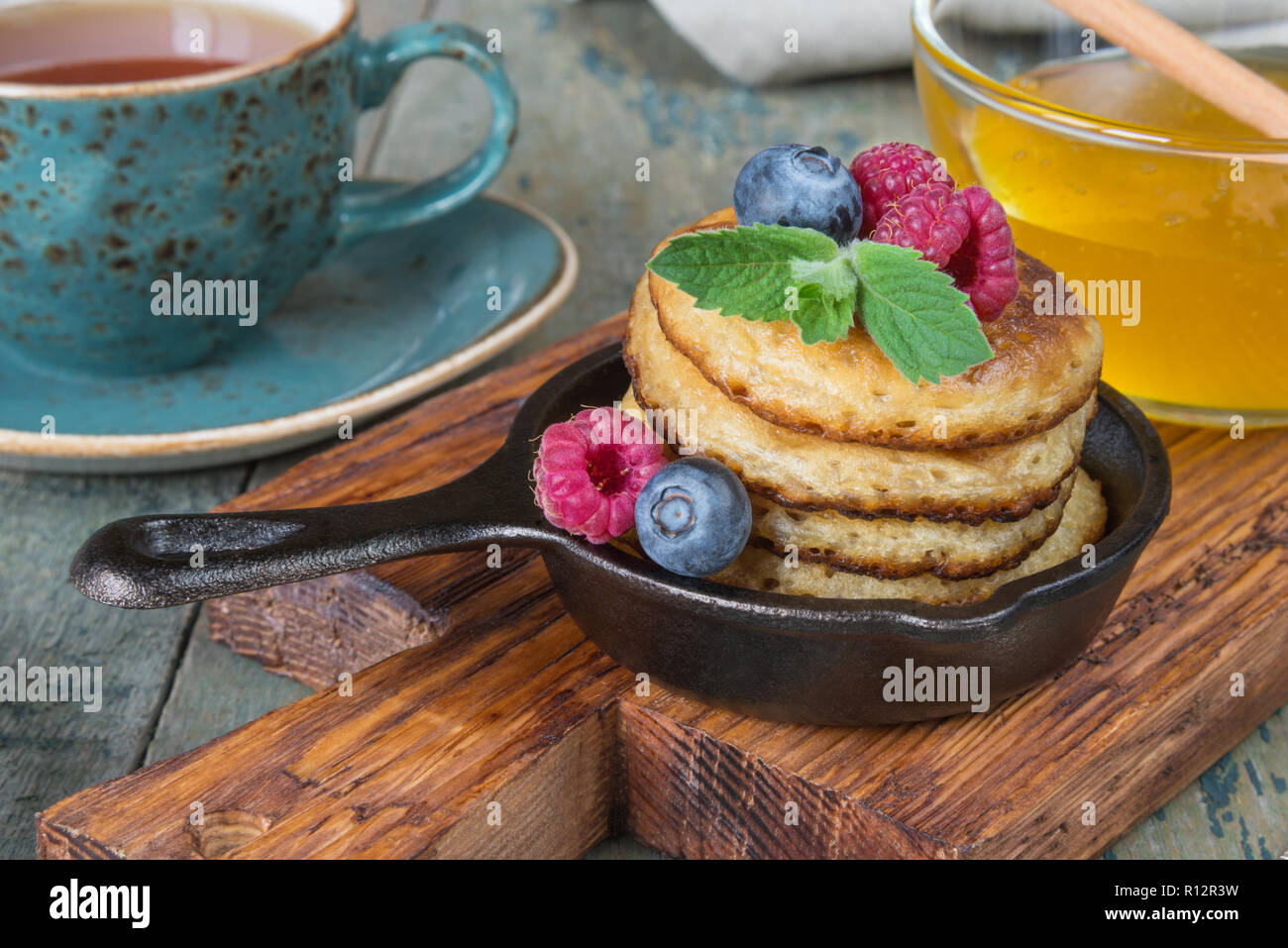 La colazione in stile rustico: frittelle in ghisa padelle, miele e frutti di bosco freschi e il tè nero Foto Stock