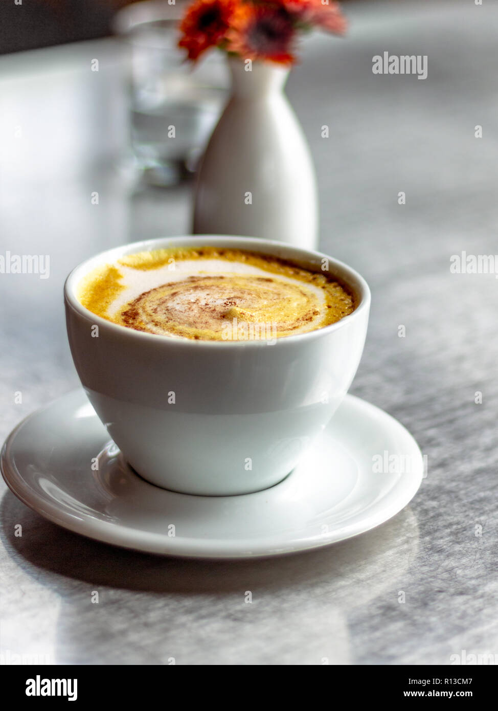 Casual caffetteria. Latte art. La formazione di schiuma del latte. Brocca in vetro chiaro. Fiori d'arancio in un bianco ovale vaso bianco. Foto Stock