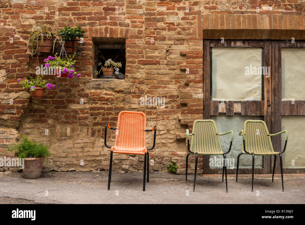 Tre sedie colorati a sinistra al di fuori di un vecchio edificio in mattoni, chiusure, un piccolo paese della provincia di Siena, Toscana, Italia Foto Stock