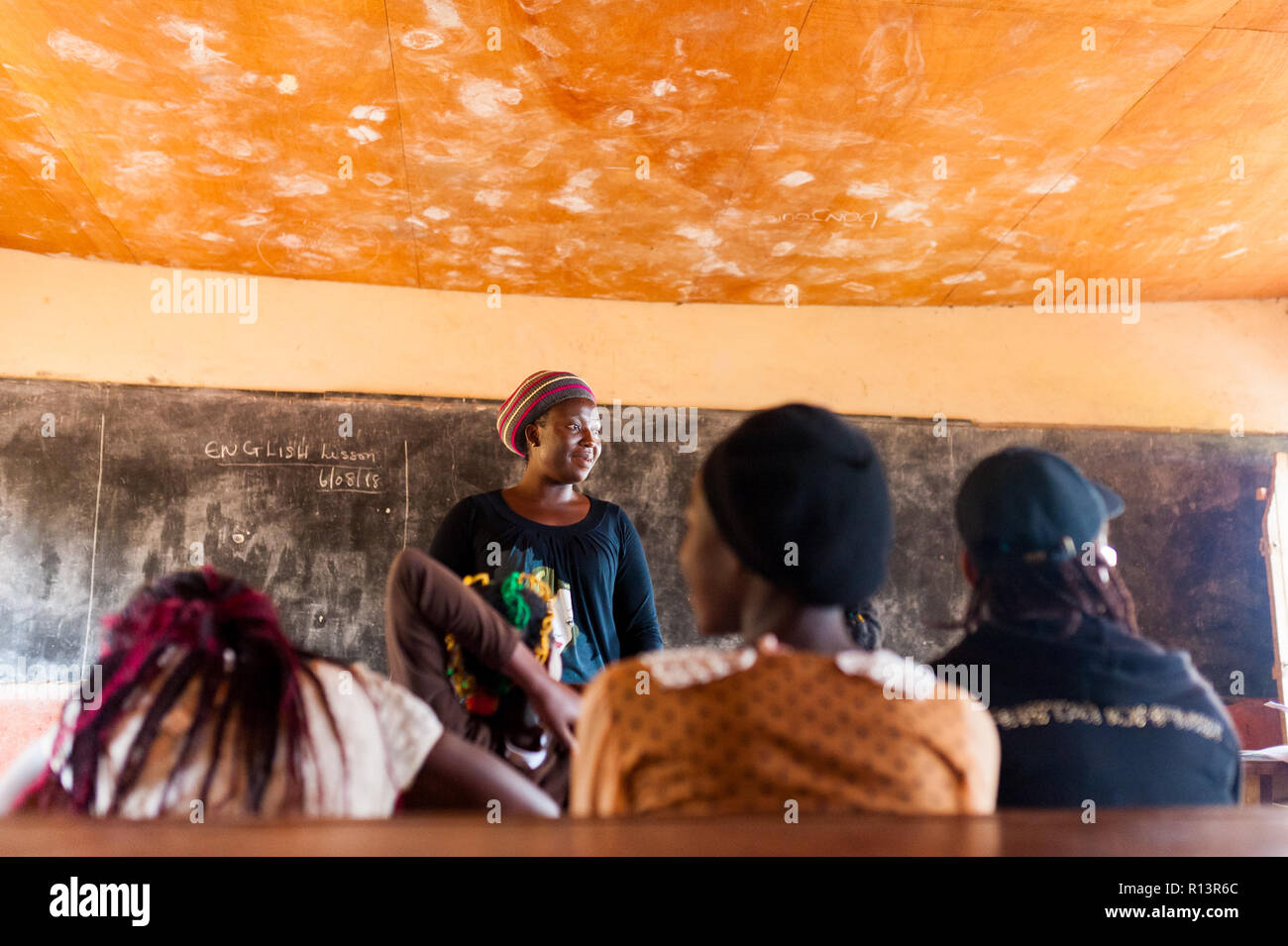 Bafoussam, Camerun - 06 agosto 2018: giovane donna africana maestro sorridente di volontariato durante la lezione di umile aula scolastica Foto Stock