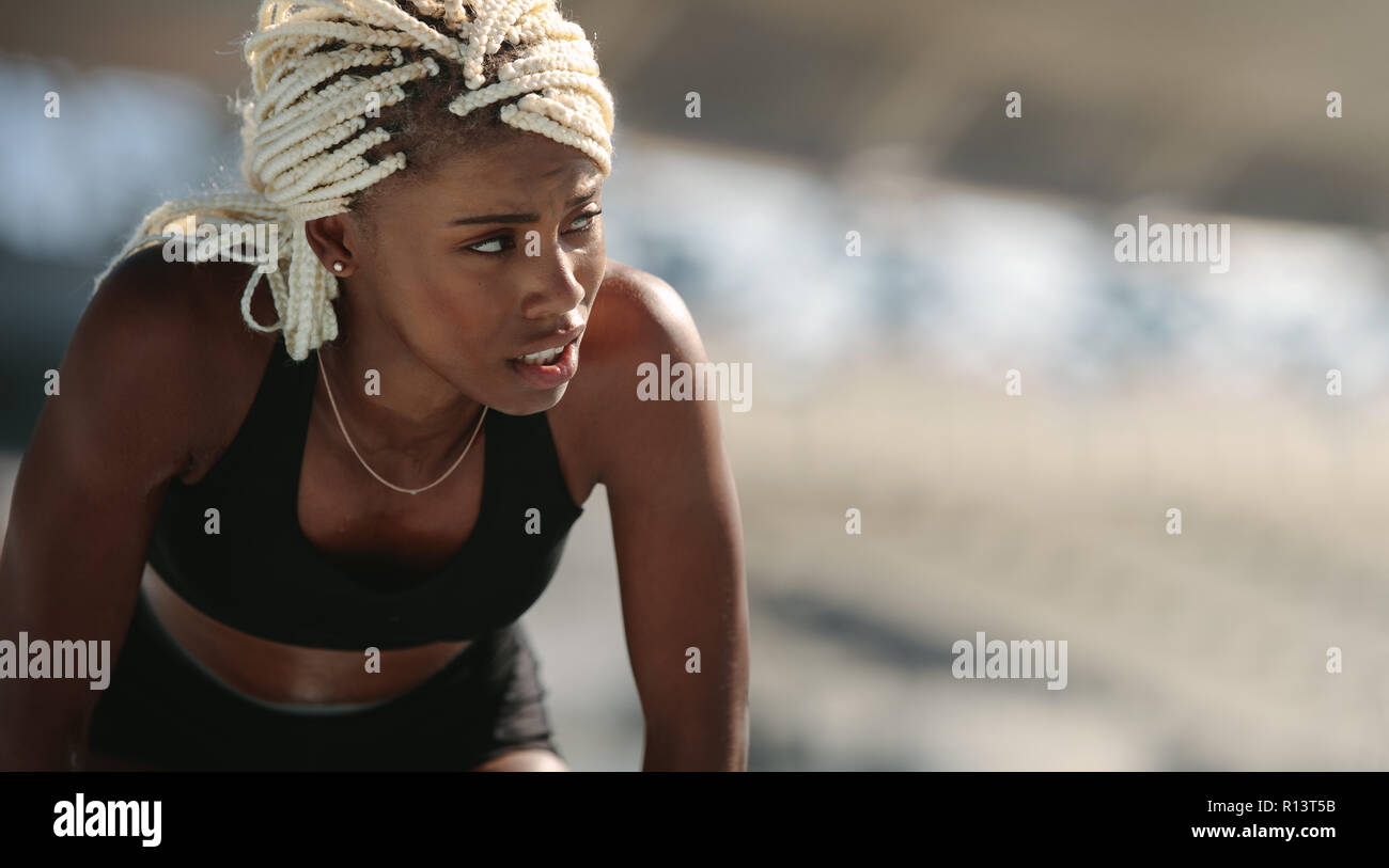 Close up di un velocista femmina in piedi all'interno di uno stadio. Stanco atleta rilassante la piegatura in avanti. Foto Stock