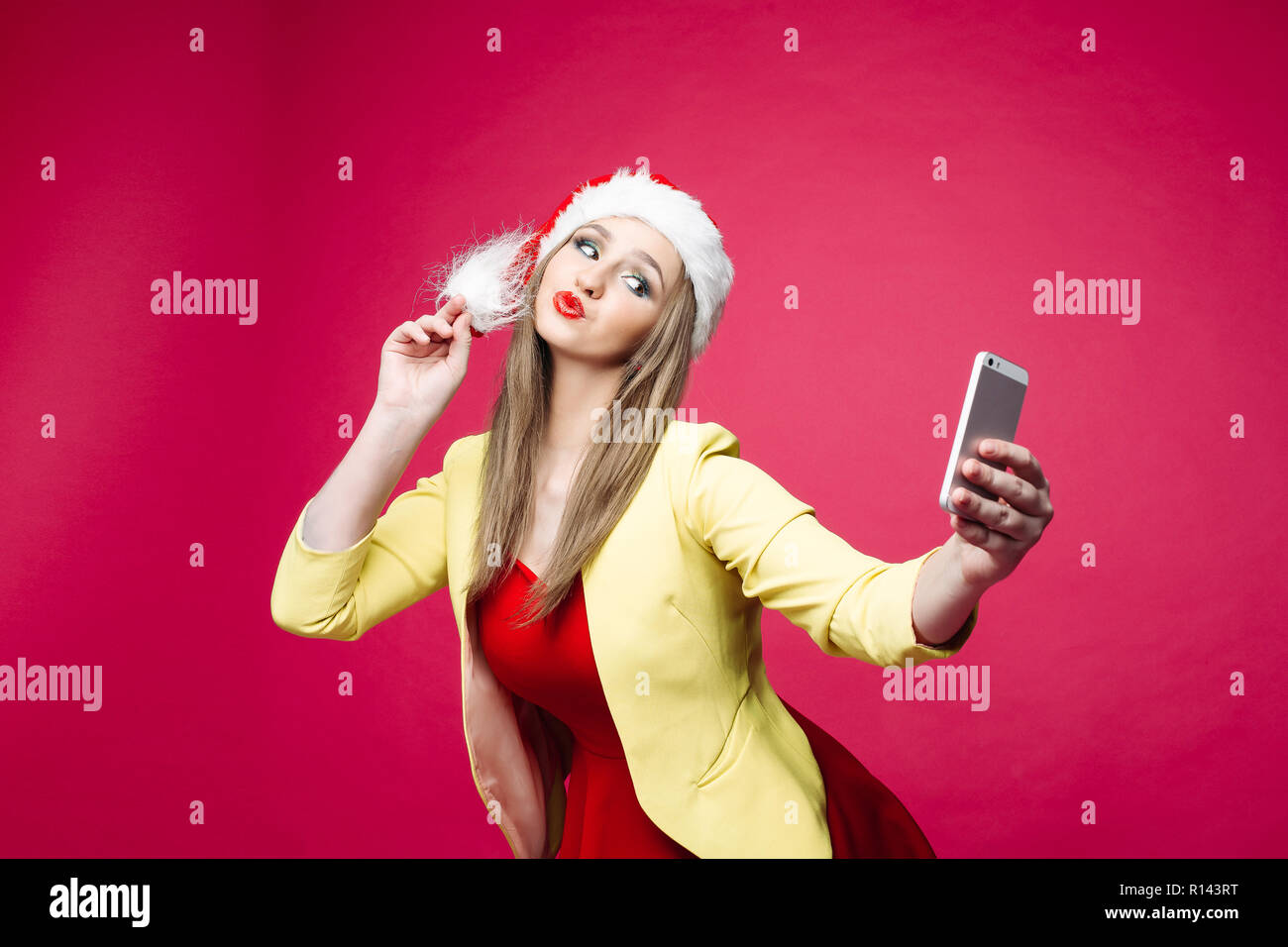 La donna sorpresa in santa hat rendendo selfie su sfondo rosa. Foto Stock