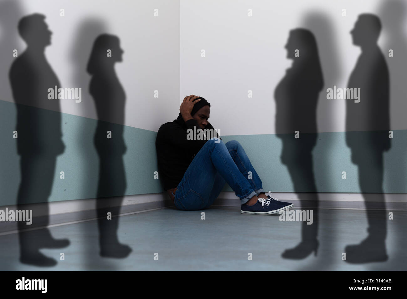 Ombre di persone in piedi vicino a paura uomo seduto sul pavimento Foto Stock