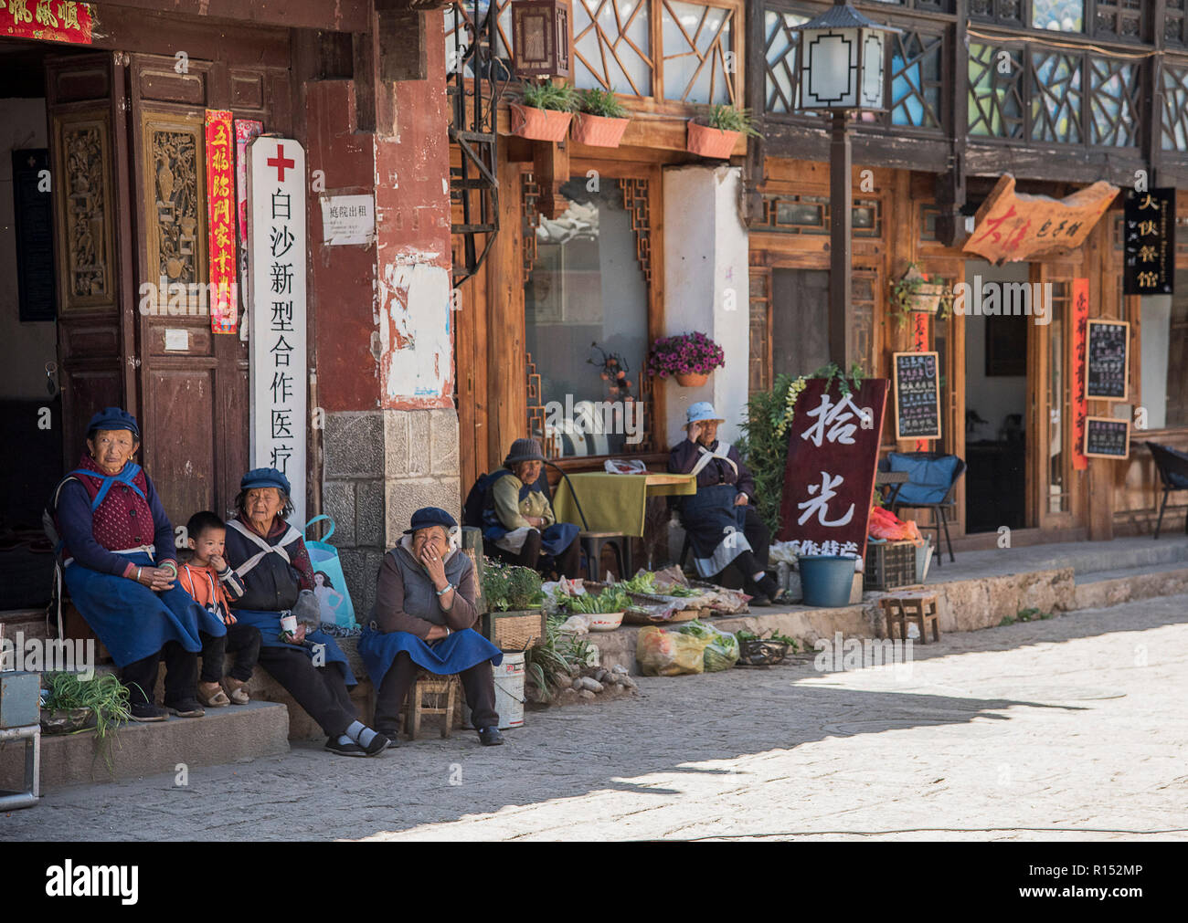 Famiglia di minoranza etnica cinese seduta al di fuori di un negozio nella città antica di Baisha sud ovest della Cina. Foto Stock