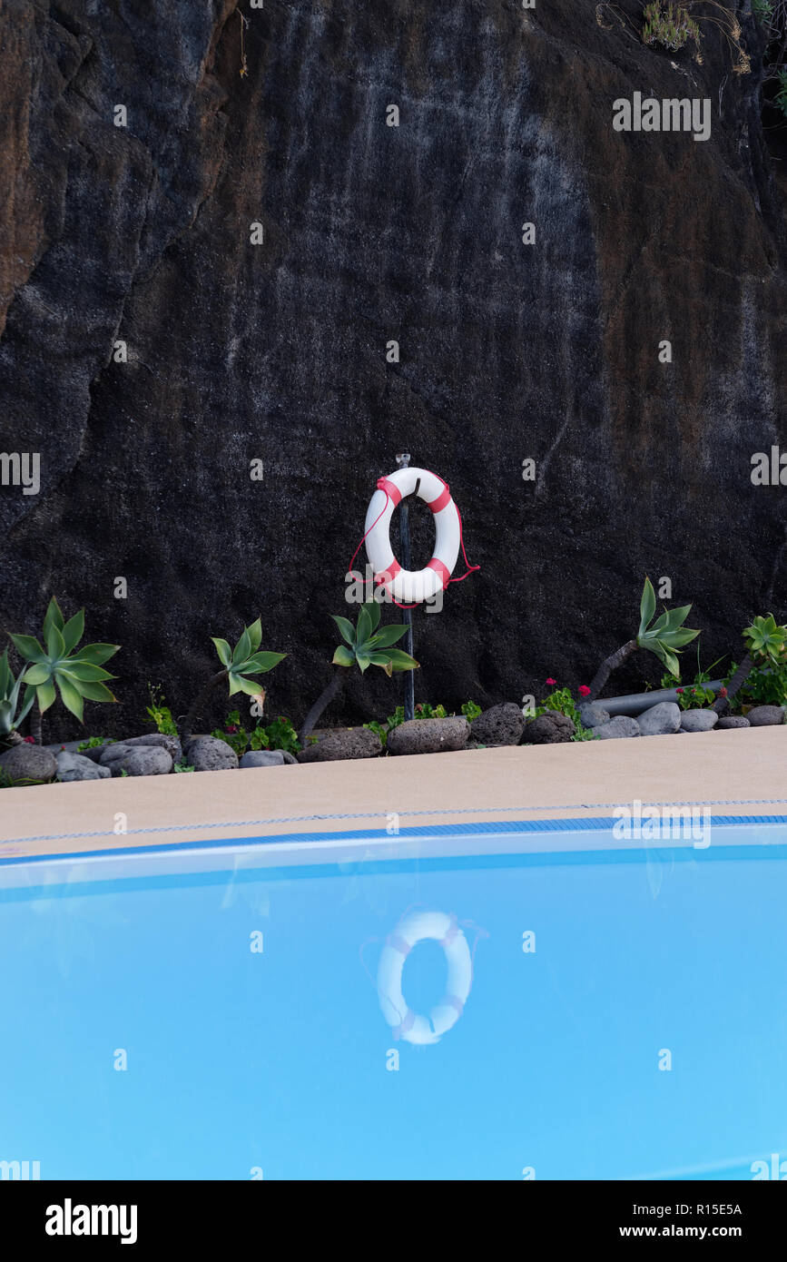 Salvagente appeso sulla scura parete rocciosa presso la piscina. Isola portoghese di Madeira Foto Stock