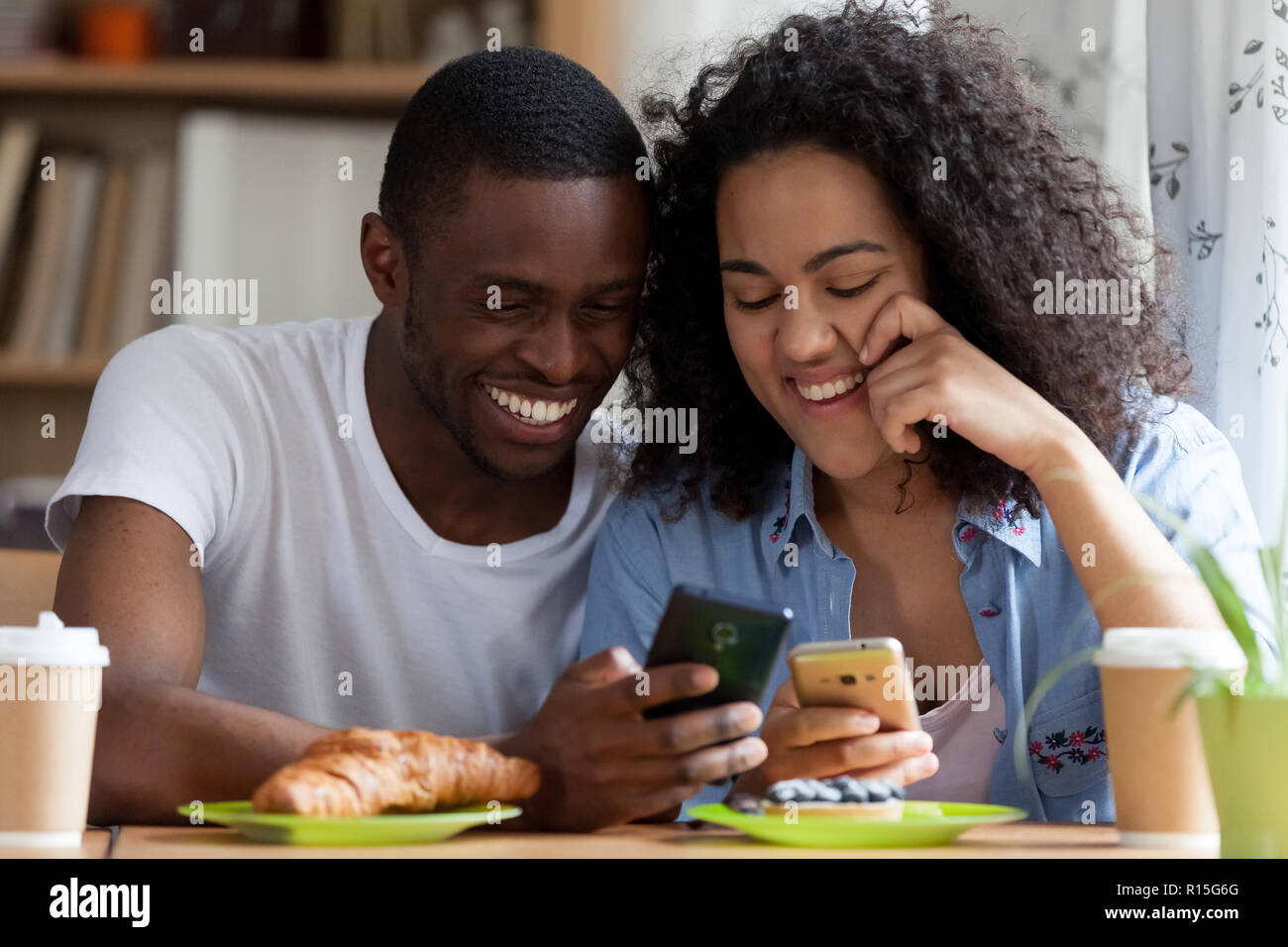 Colpo alla testa nero ritratto ragazzo e ragazza biracial matura in amore seduti insieme a tavola in cafe bere il caffè mangiare dolci. Paio utilizzando shari cellulare Foto Stock