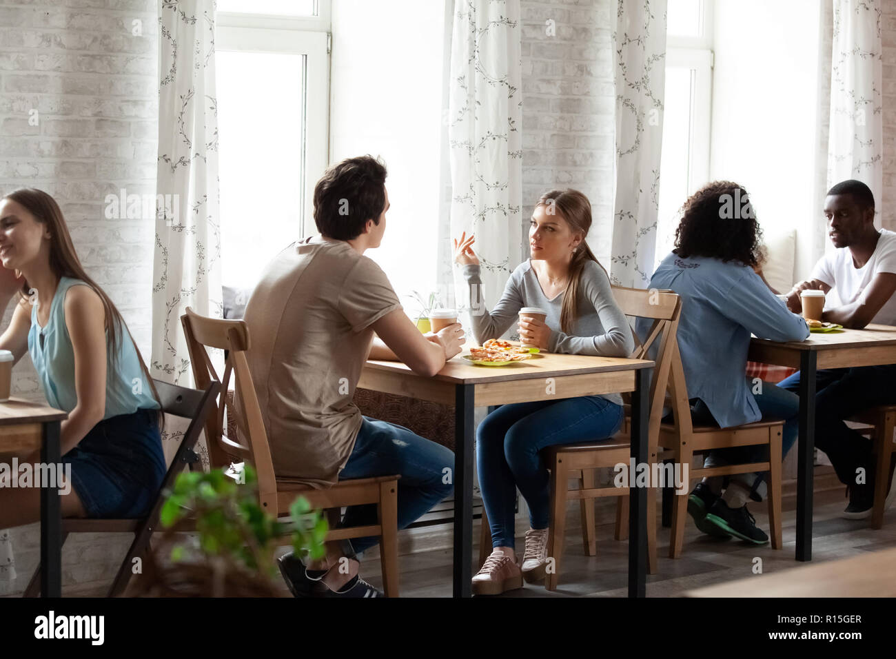 Interno della cafeteria accogliente con sedie di legno Tavoli in fila, diverse multi-etnico coppie di innamorati o migliori amici seduti a bere caffè godendo assortiti Foto Stock