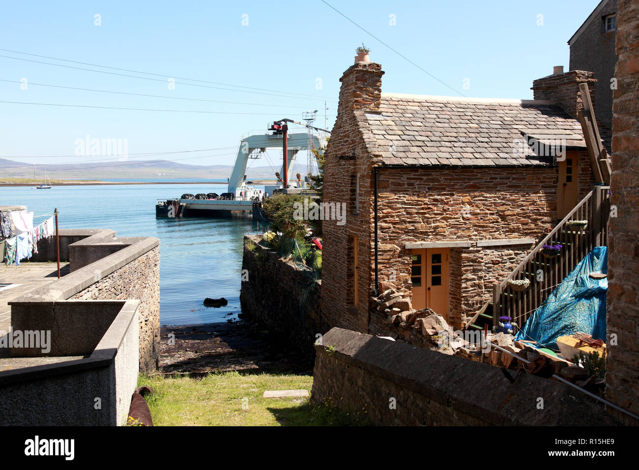 Una sorta di scivolo accanto ad una tradizionale casa sul lungomare e di un catamarano gantry Barge in porto, Stromness, Orkney. Foto Stock