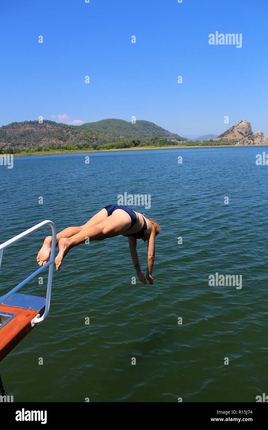 Femmina caucasica salti turistico/immersioni fuori da una barca in acqua a Dalyan, Turchia. Foto Stock