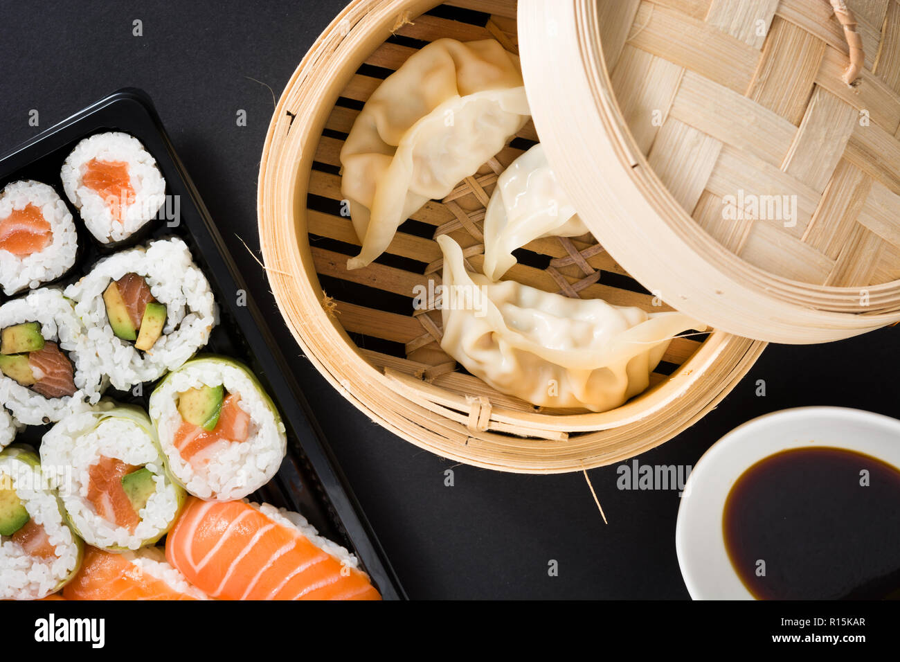 Canederli o gyoza serviti nel tradizionale sistema di cottura a vapore e sushi su sfondo nero. Laici flat top-down composizione Foto Stock