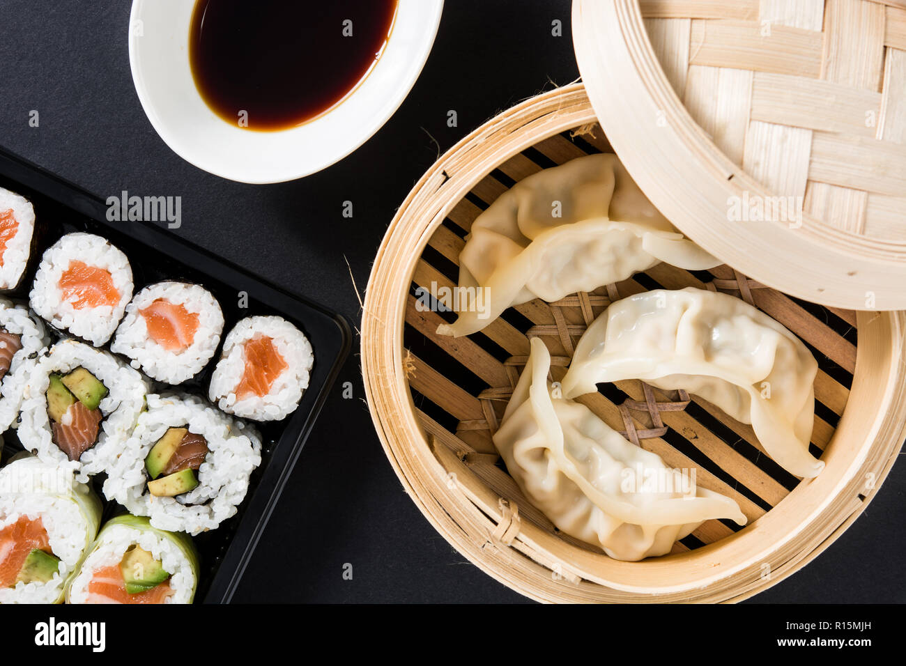Canederli o gyoza serviti nel tradizionale sistema di cottura a vapore e sushi su sfondo nero. Laici flat top-down composizione Foto Stock
