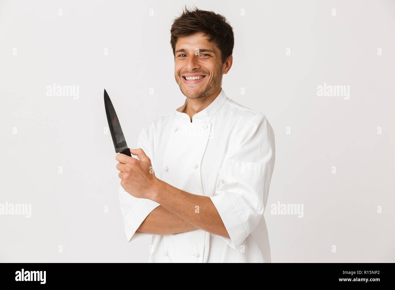 Immagine del bel giovane chef man standing isolate su muro bianco sullo sfondo tenendo il coltello. Foto Stock
