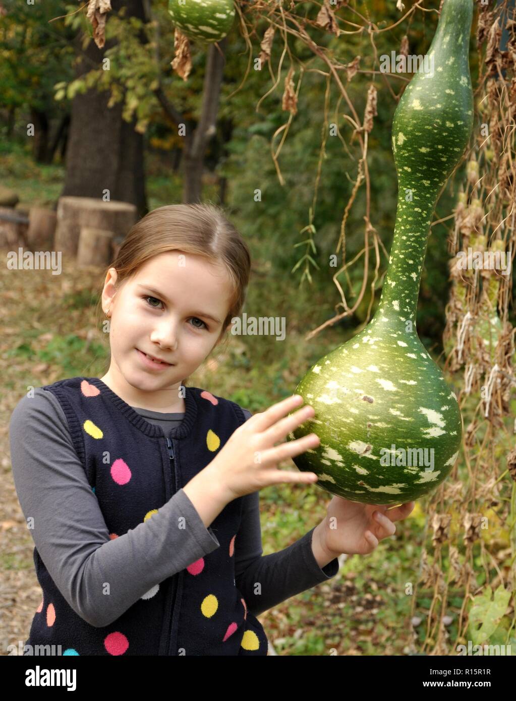 Caucasian 8 anni bambino, ragazza, felice nel parco, sorridente e tenendo una bottiglia di zucca. In verticale Foto Stock
