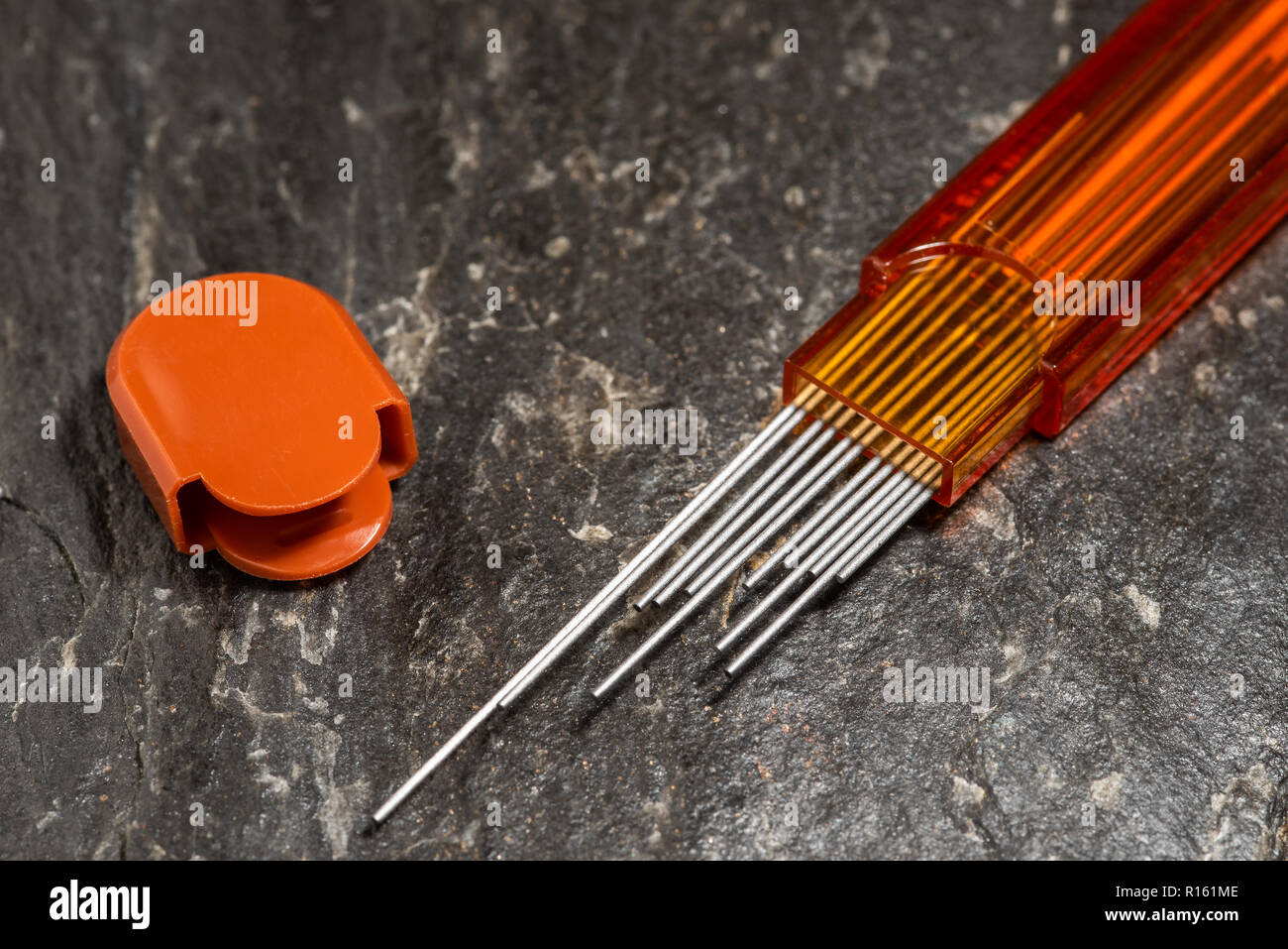 Matita di scorta conduce in aprire la cartuccia di colore arancione, coperchio accanto, su sfondo di pietra. Foto Stock