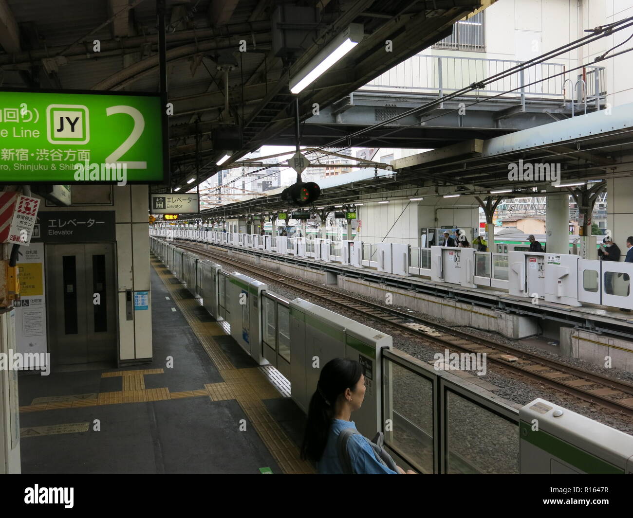Una donna attende passeggero dalle barriere automatiche sulla piattaforma della linea Yamanote (JR East) alla stazione di Tokyo; Giappone Foto Stock