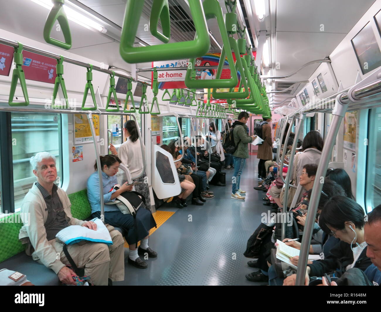Vista interna di un treno di trasporto sulla Linea Yamanote (JR East) da Tokyo a Meguro; maniglie verdi appesi al soffitto per i passeggeri in piedi Foto Stock