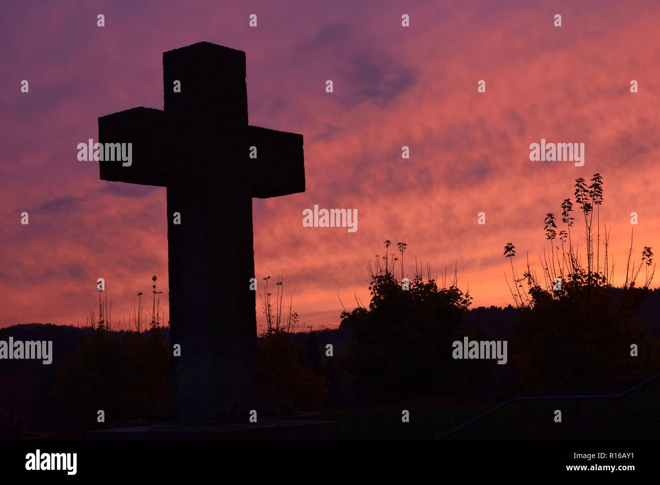 Time-lapse del sole al tramonto di sera Cielo di tramonto visto da dietro una pietra arenaria rossa croce durante l'impostazione di Sun nel cimitero civile Reimsbach Foto Stock