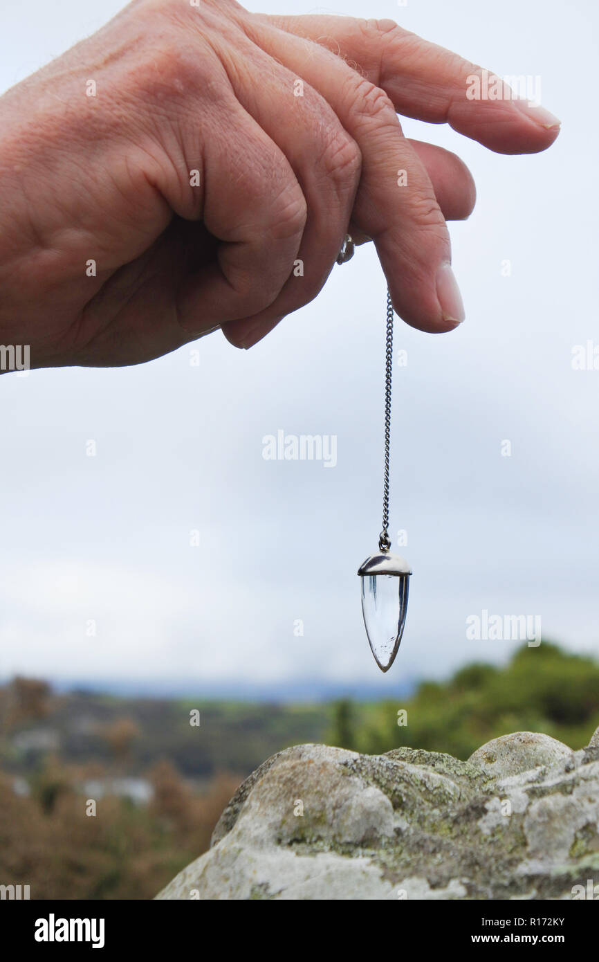 Maschio lato tenendo in mano un cristallo pendolo radioestesia la parte superiore di una pietra permanente, Ardgroom, County Cork, Irlanda - Giovanni Gollop Foto Stock