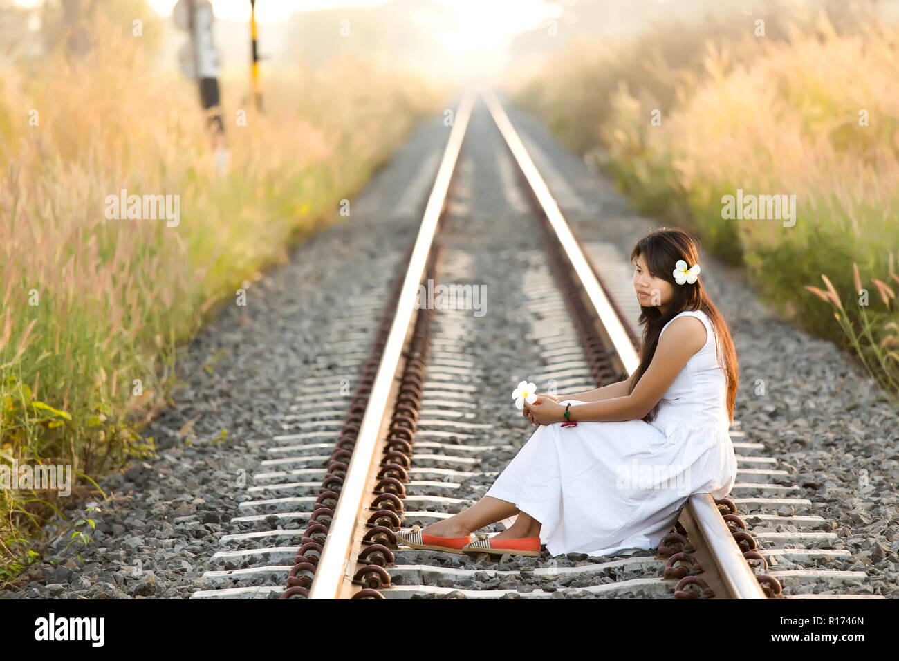 Bellissima giovane donna Thai seduti in meditazione nel gli ultimi raggi di sole su un treno sfuggente via in un nuovo abito bianco con un espressione serena un Foto Stock