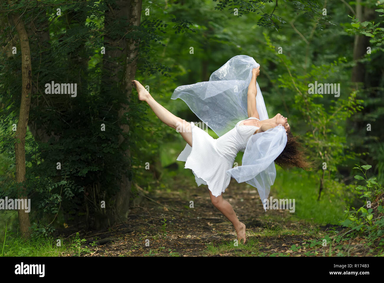 Ritratto di mistica di un grazioso bella donna a piedi nudi in un nuovo abito bianco con le braccia drappeggiati in annebbiato tessuto di pura e semplice posa con una gamba sollevata Foto Stock