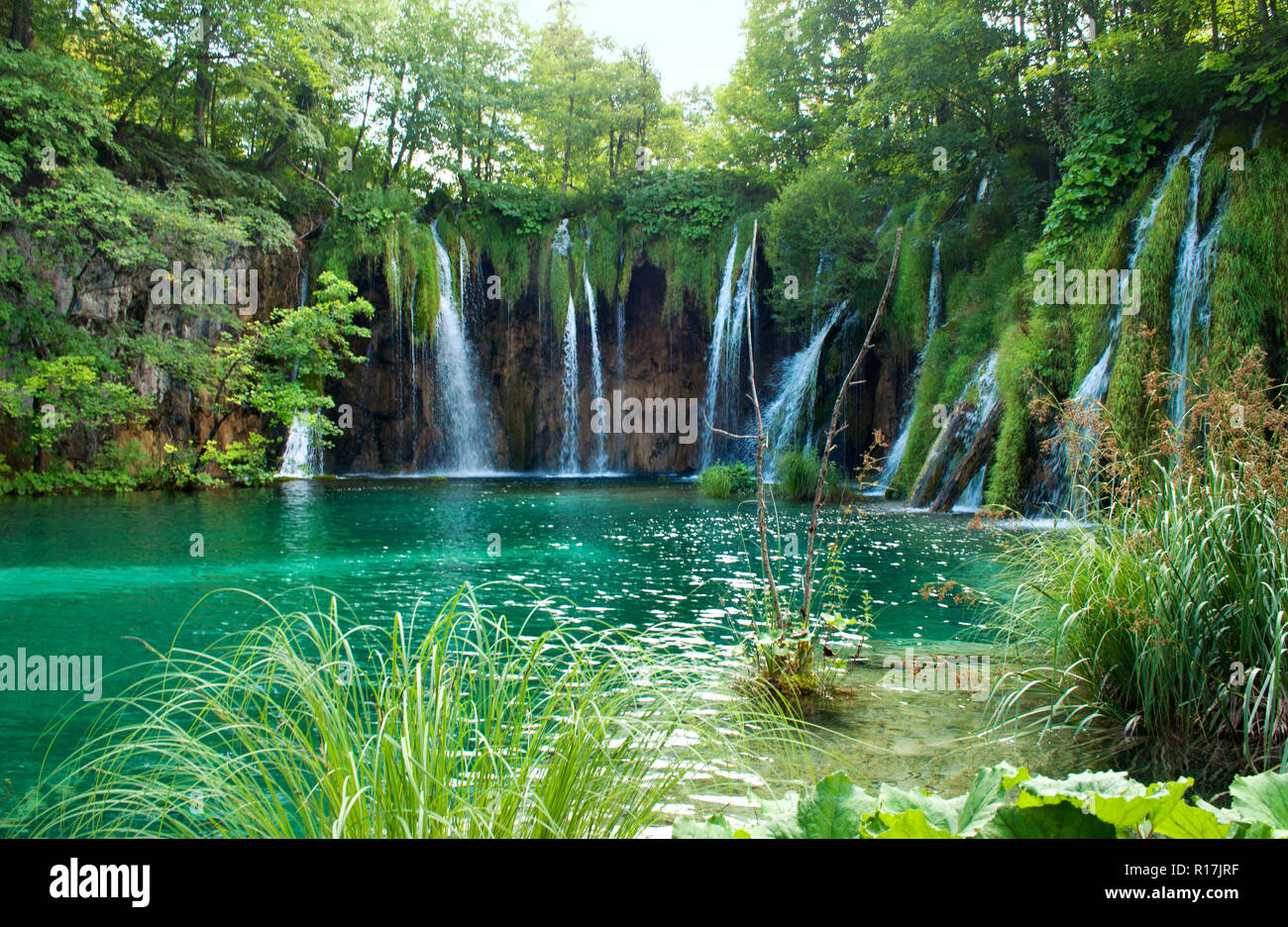 Lago con trasparente di acqua color smeraldo. Cascata tra le rocce rosse e il fogliame. Il parco nazionale dei laghi di Plitvice, Croazia Foto Stock
