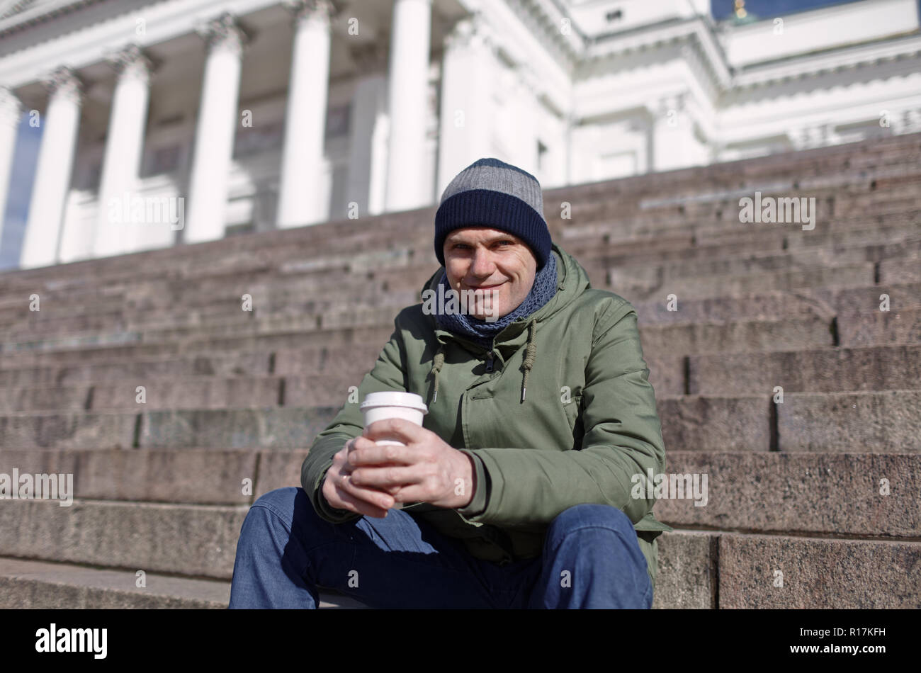 Uomo in abbigliamento invernale con una tazza di caffè seduti sulla scalinata della Cattedrale di Helsinki Foto Stock
