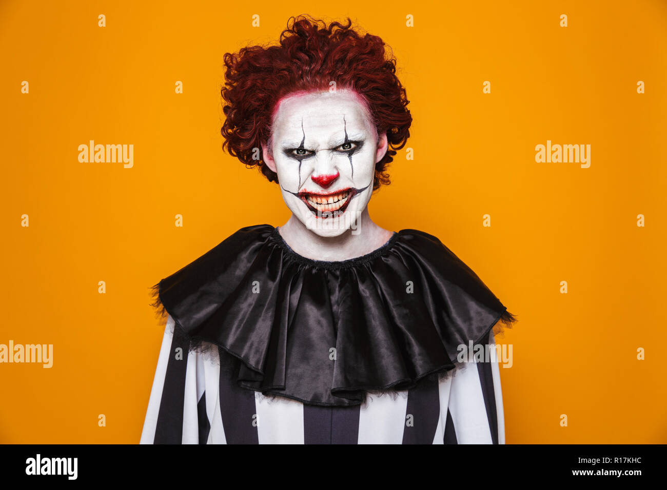 Angry clown uomo 20s indossando il costume nero e Halloween trucco guardando la telecamera isolate su sfondo giallo Foto Stock