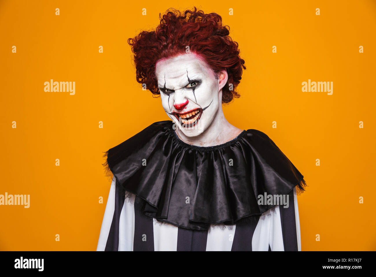 Irritato clown uomo 20s indossando il costume nero e Halloween trucco guardando la telecamera isolate su sfondo giallo Foto Stock