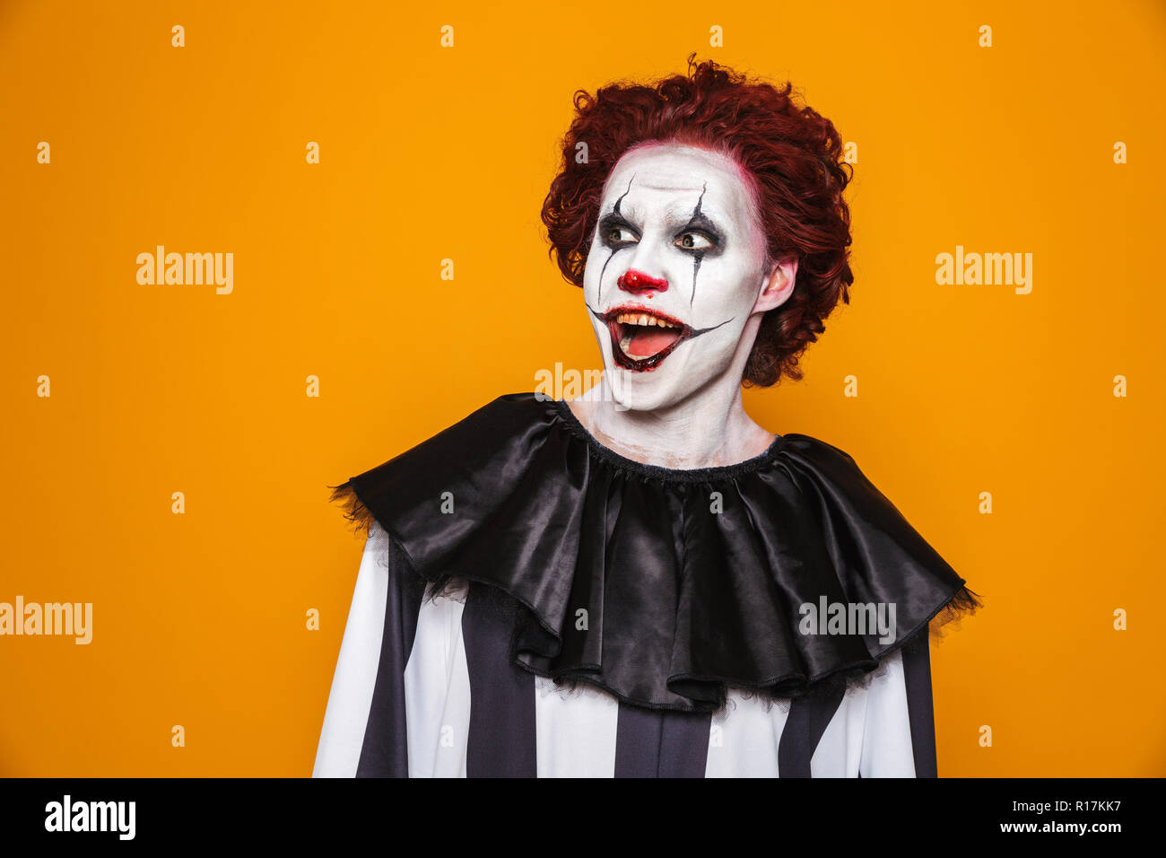 Sorpreso clown uomo 20s indossando il costume nero e Halloween trucco cercando riposo isolate su sfondo giallo Foto Stock