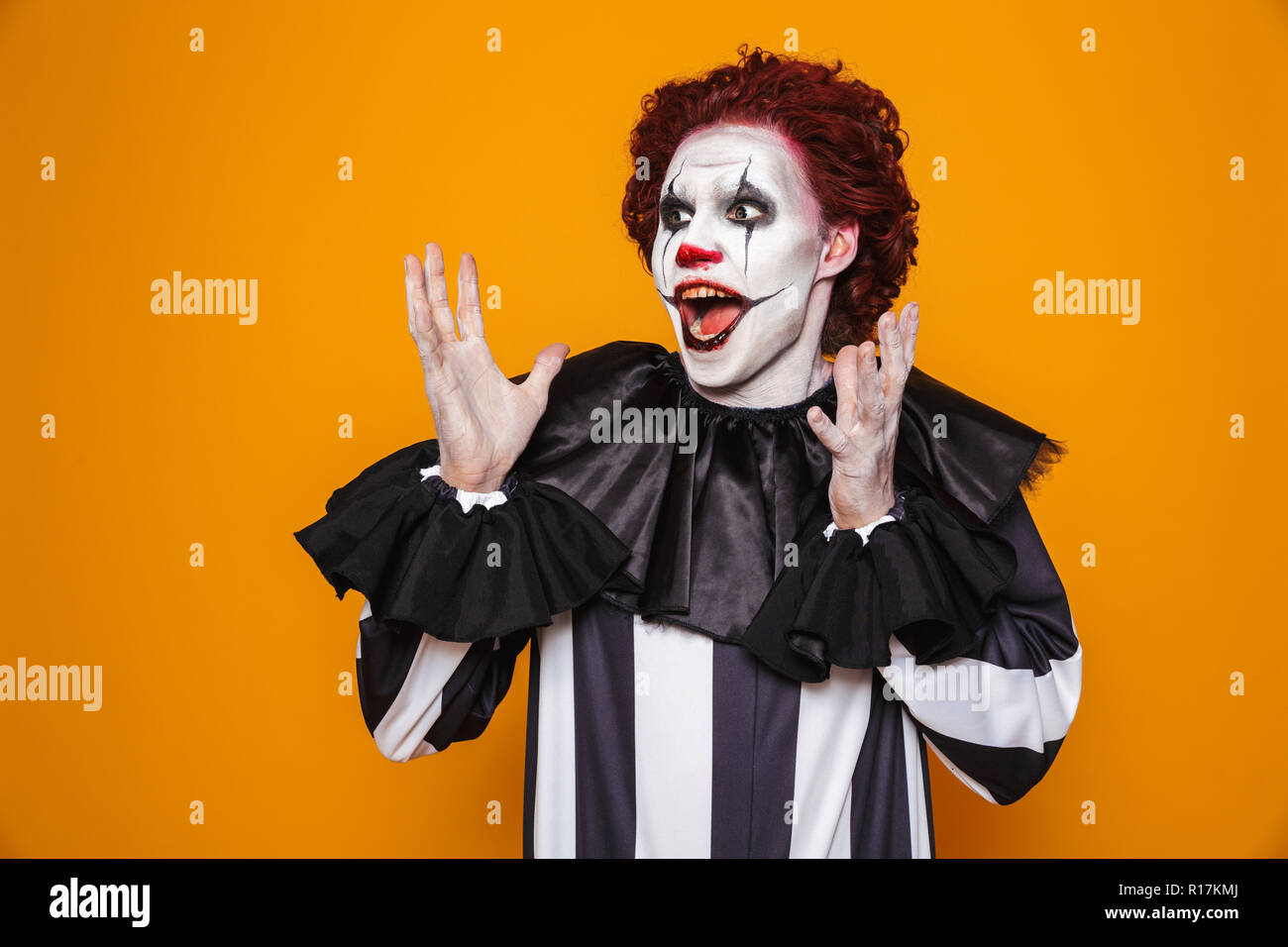 Scioccato clown uomo 20s indossando il costume nero e Halloween trucco cercando riposo isolate su sfondo giallo Foto Stock
