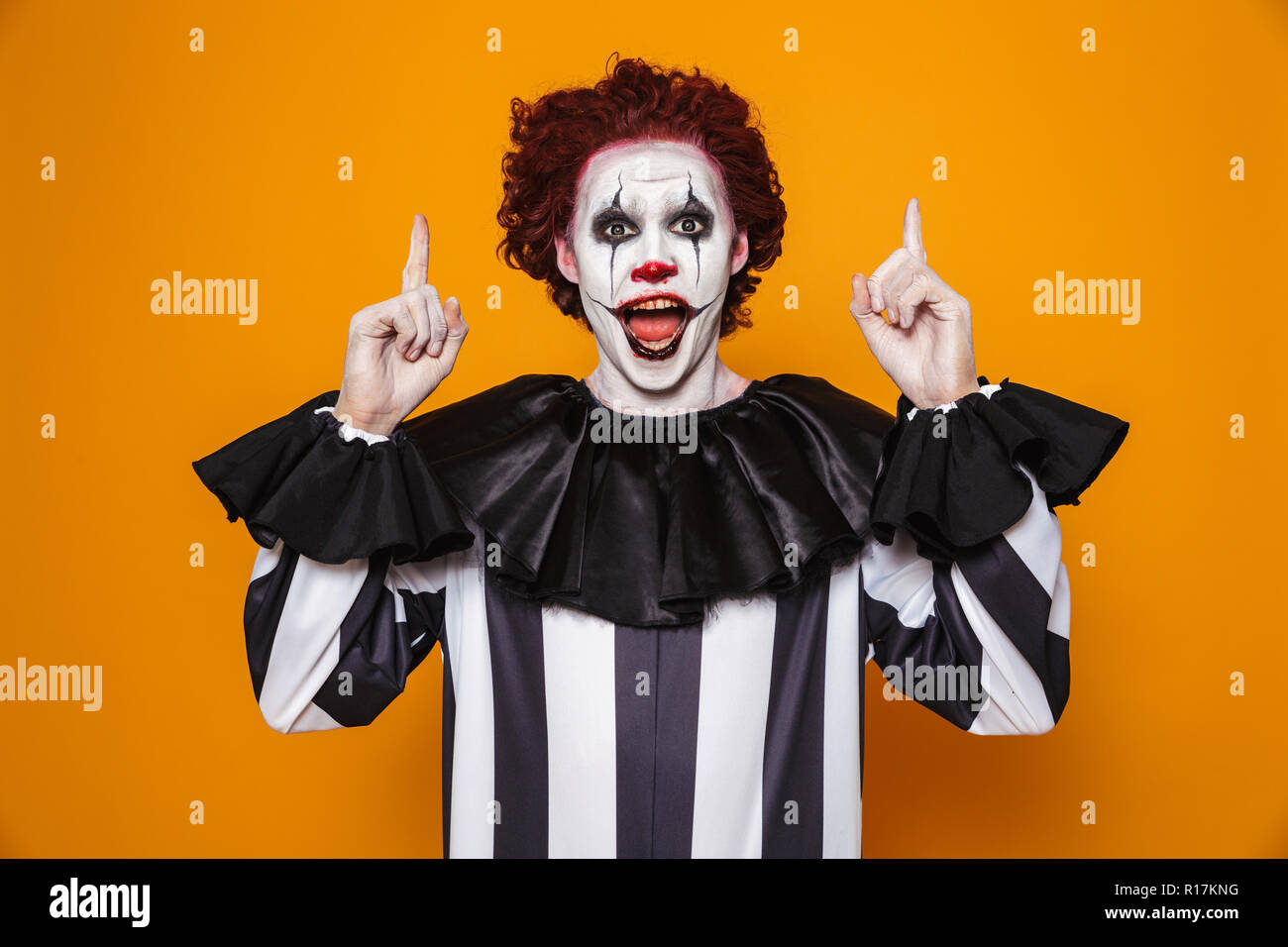 Felice l'uomo clown 20s indossando il costume nero e Halloween trucco guardando la telecamera isolate su sfondo giallo Foto Stock