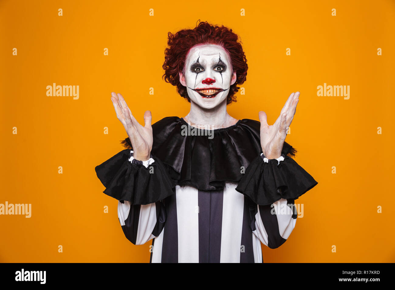 Giovane uomo clown 20s indossando il costume nero e Halloween trucco guardando la telecamera isolate su sfondo giallo Foto Stock