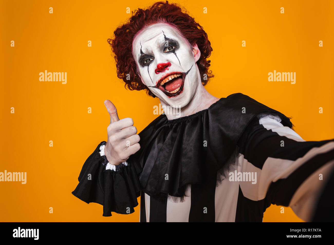 Excited clown uomo 20s indossando il costume nero e Halloween trucco guardando la telecamera isolate su sfondo giallo Foto Stock