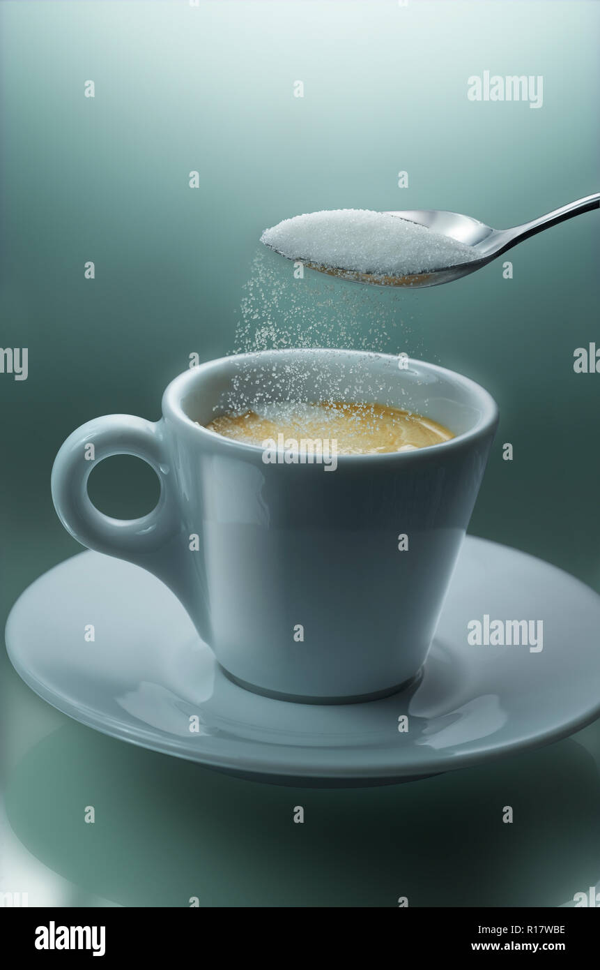 Versare lo zucchero da cucchiaino nella tazza di caffè, sfondo semplice Foto Stock