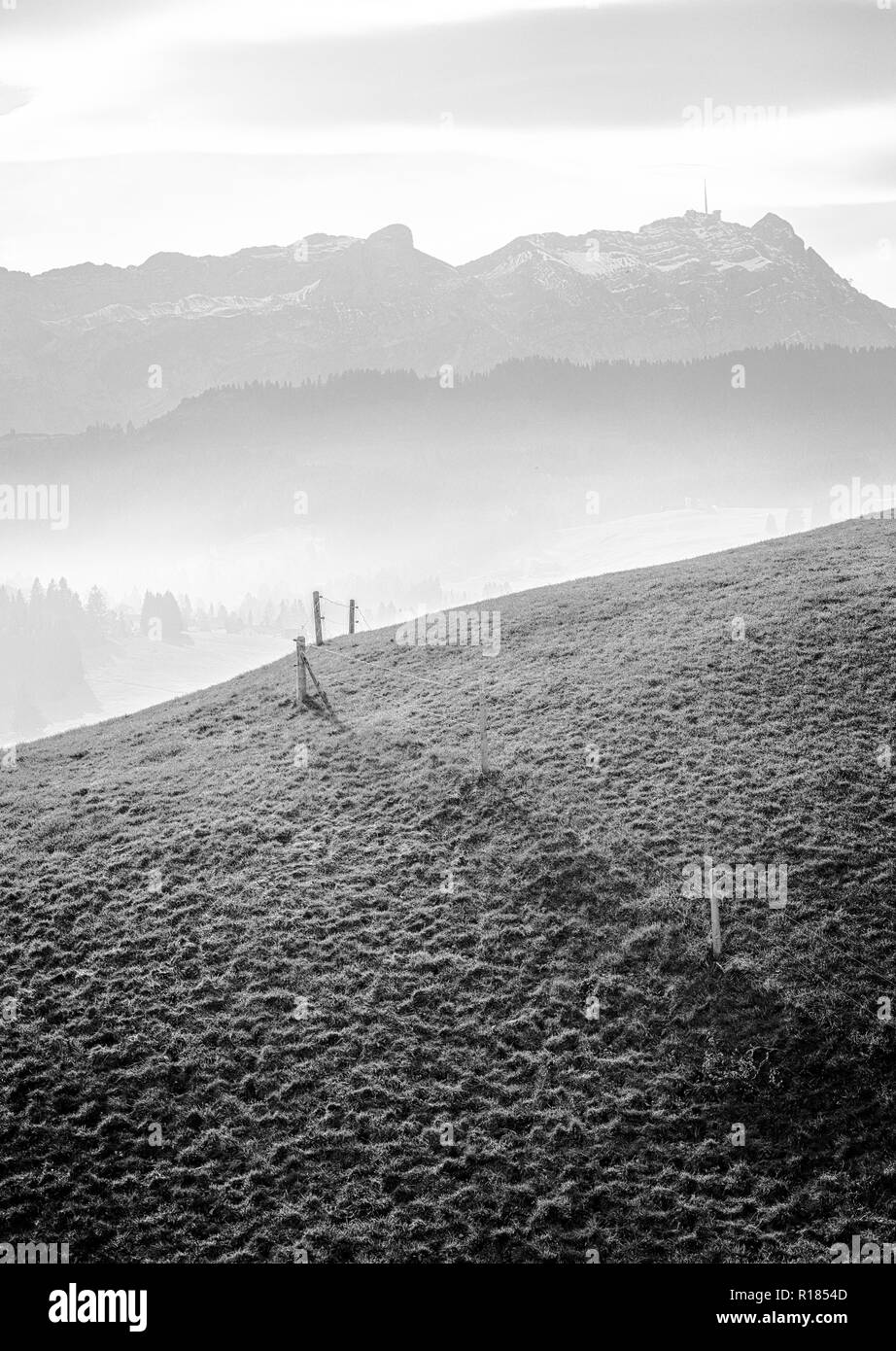 Idilliaco e tranquillo paesaggio di montagna con una staccionata in legno su un pendio erboso e una magnifica vista delle Alpi Svizzere dietro Foto Stock