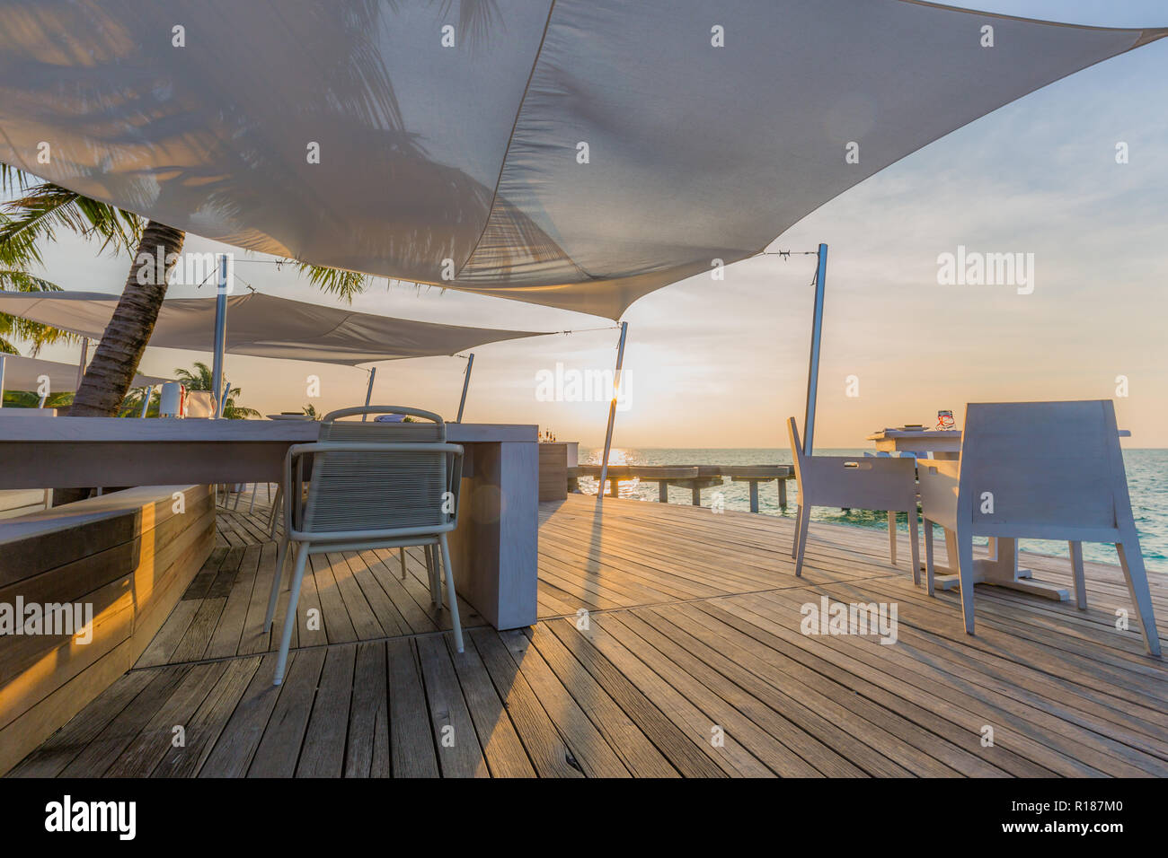 Ristorante sulla spiaggia esterno in scena al tramonto, sedie e tavolo e moderno resort tropicale o hotel all'aperto Foto Stock
