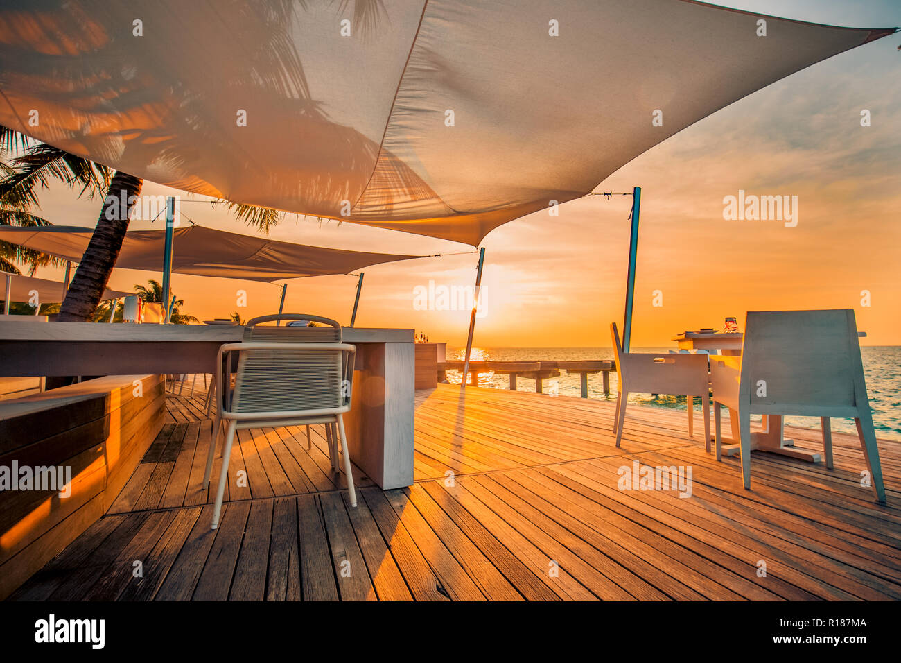 Ristorante sulla spiaggia esterno in scena al tramonto, sedie e tavolo e moderno resort tropicale o hotel all'aperto Foto Stock
