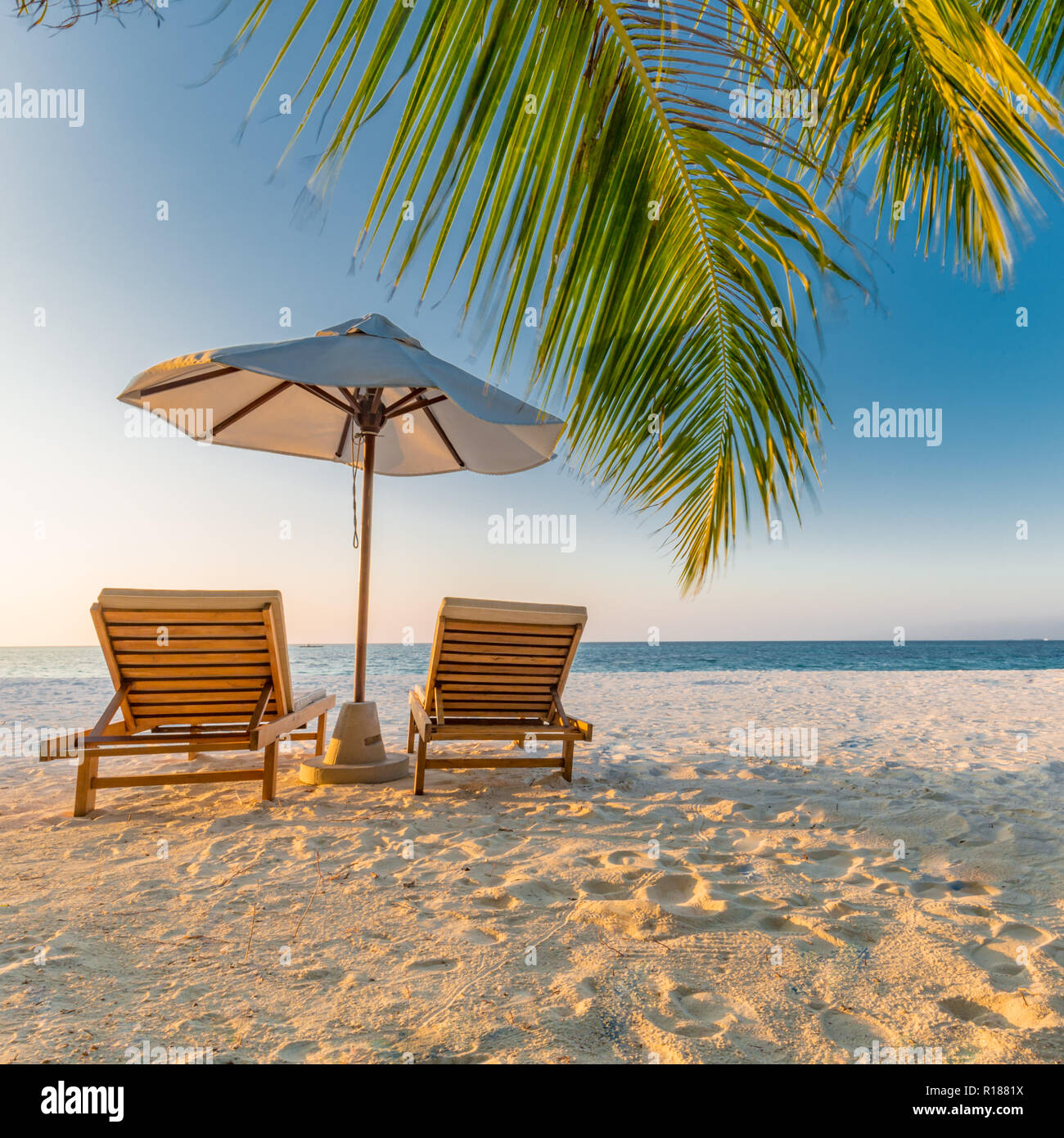 Bellissimo tramonto tropicale paesaggio, due lettini, sdraio, ombrellone sotto il palm tree. Resort di lusso, paesaggio di spiaggia con sabbia bianca e palme Foto Stock