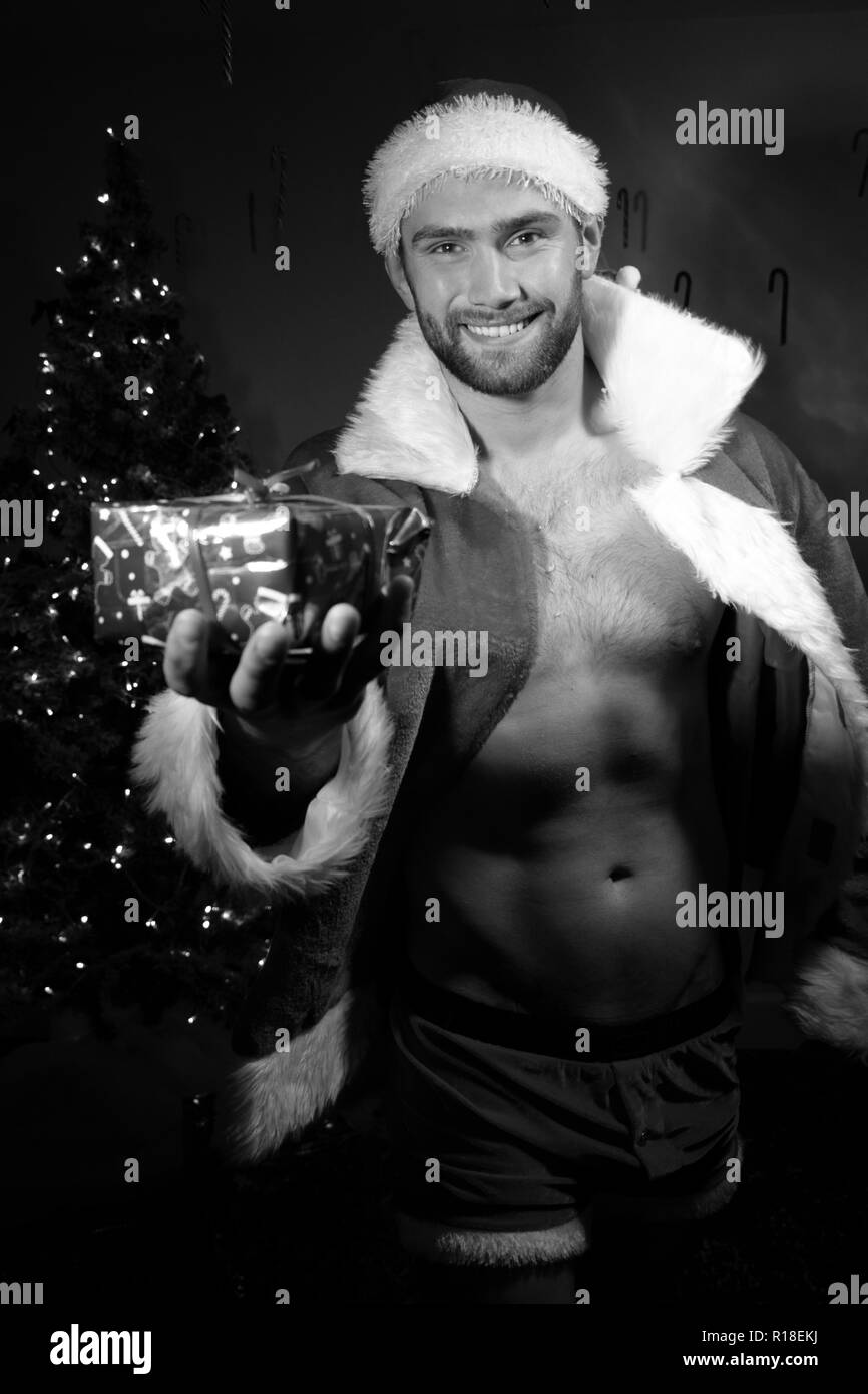 Ritratto in bianco e nero di sorridere bello maschio santa con camicia aperta tenendo in mano un regalo di Natale Foto Stock