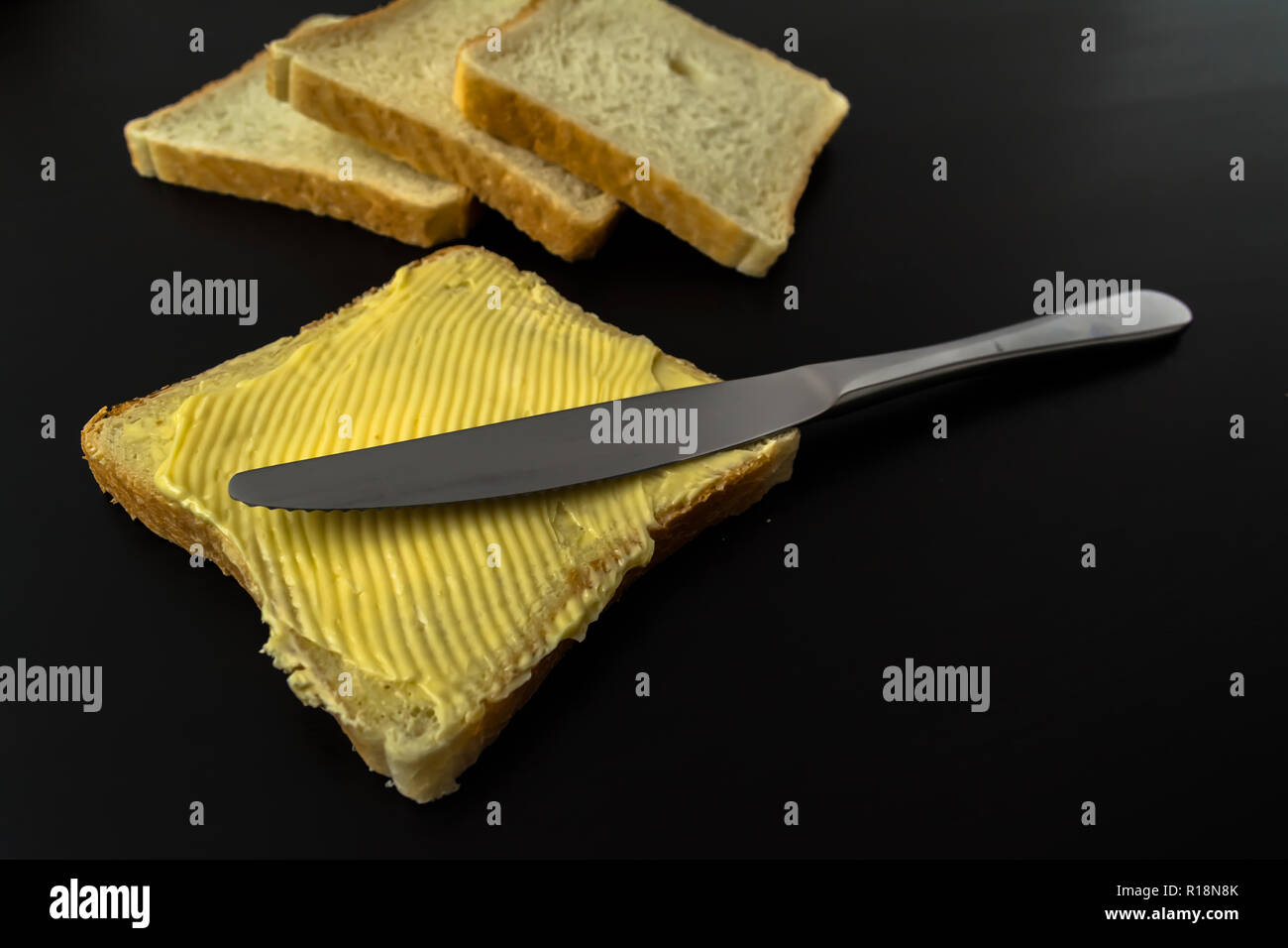 Il burro con belle macchie e un coltello su un pezzo di pane di close-up su sfondo scuro Foto Stock