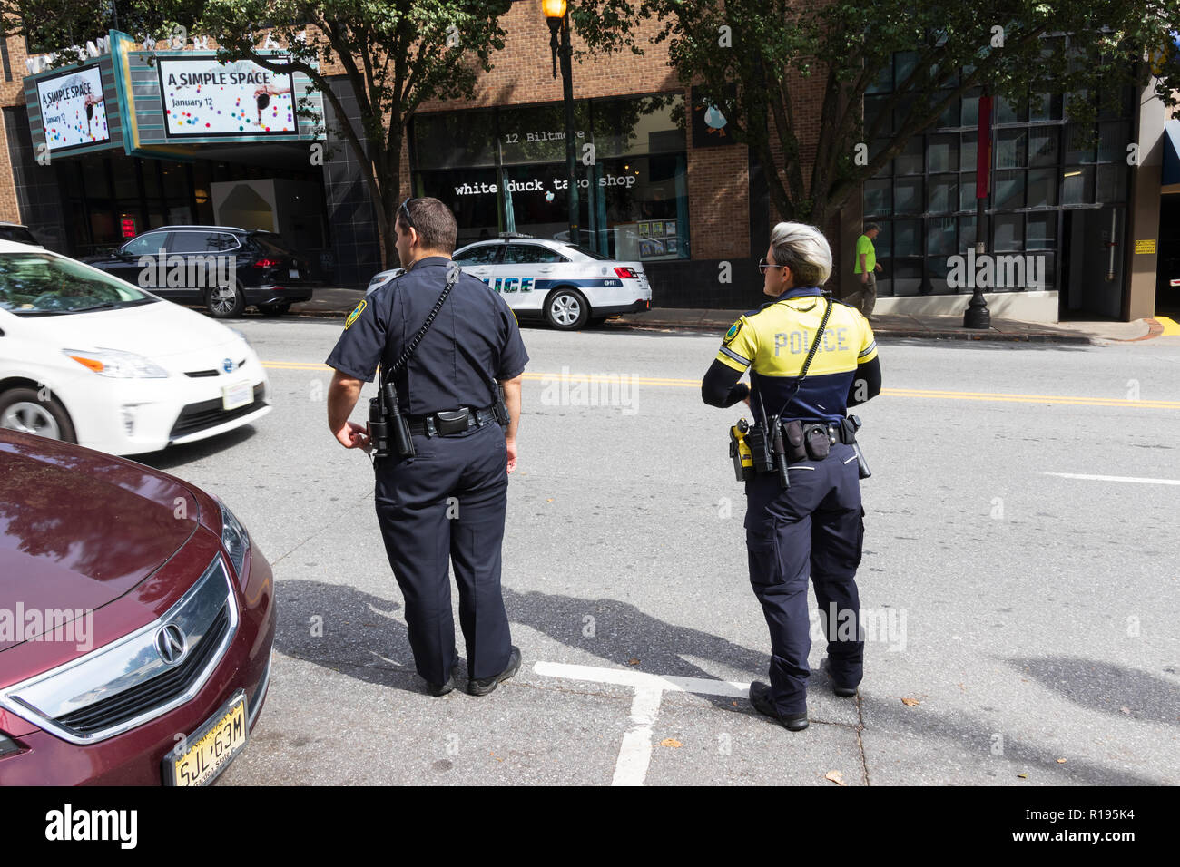 ASHEVILLE, NC, Stati Uniti d'America 10/17/18: due funzionari di polizia, uomo e donna, attendere per attraversare Haywood Avenue. Foto Stock
