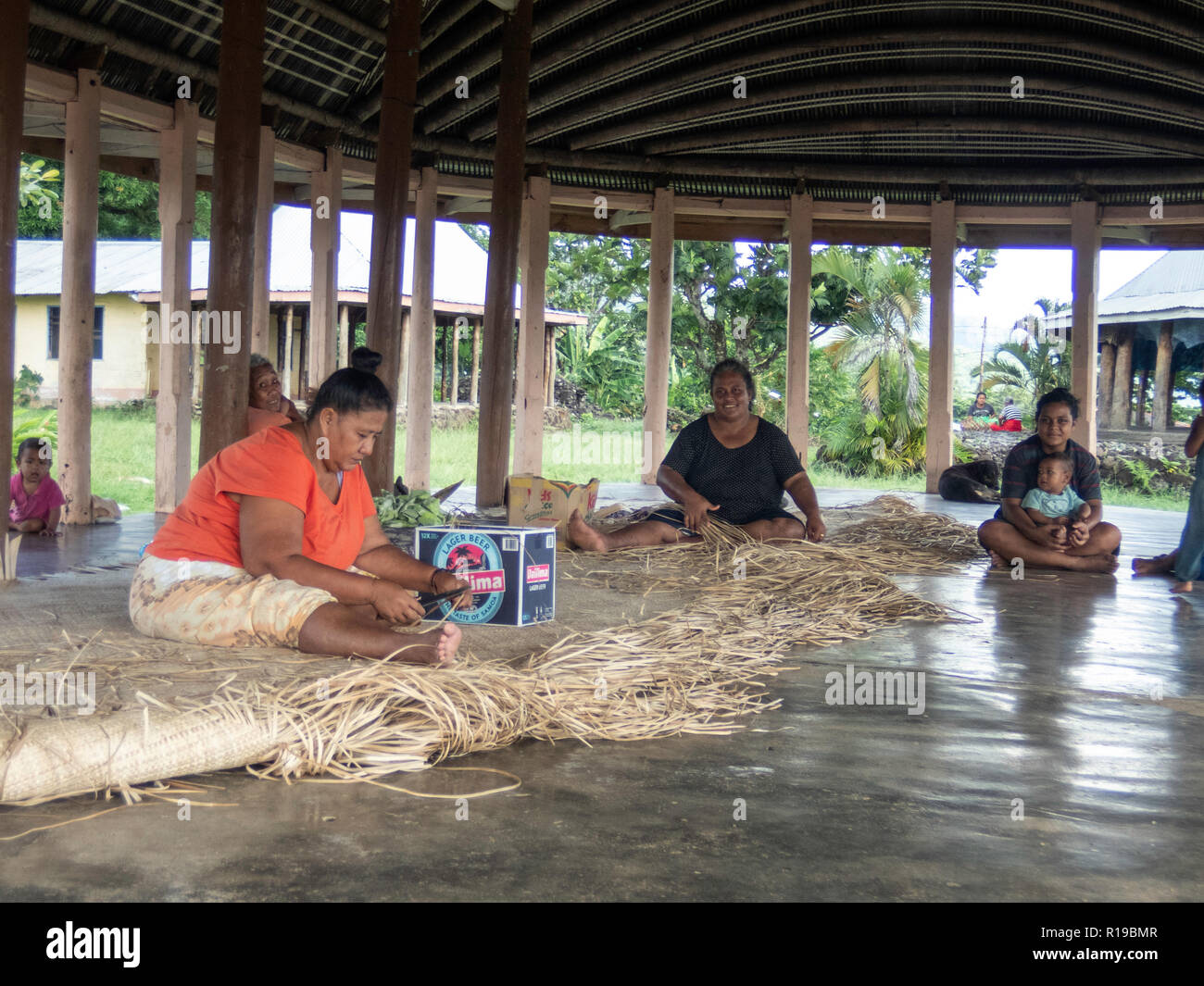 Donne con bambini di tessitura tappeti tradizionali nella città di Lufilufi sull'isola di Upolu, Samoa. Foto Stock