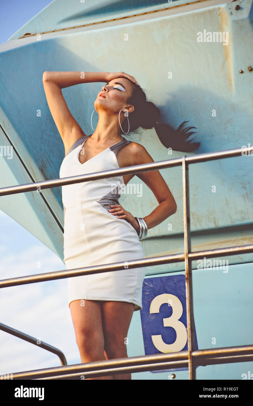 Una bella asiatica modello femminile, razza mista, in posa su un bagnino post, un esterno di moda concetto editoriale. Foto Stock