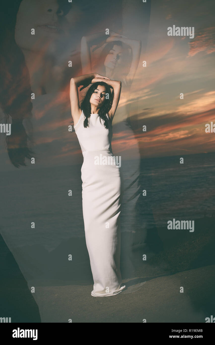 Un bellissimo modello femminile, asiatici, razza mista modello, la modellazione di un semplice abito bianco, un editoriale di moda stile di vita outdoor concept contro un cielo scuro. Foto Stock