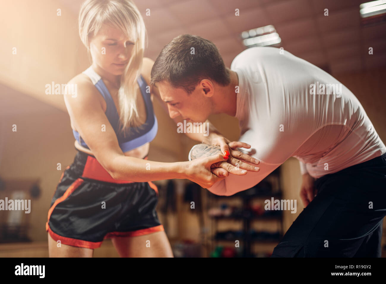 Persona di sesso femminile rende doloroso presa della mano, auto-difesa allenamento con connettore maschio di tipo personal trainer, palestra interno su sfondo. Donna sulla difesa di auto in treno Foto Stock