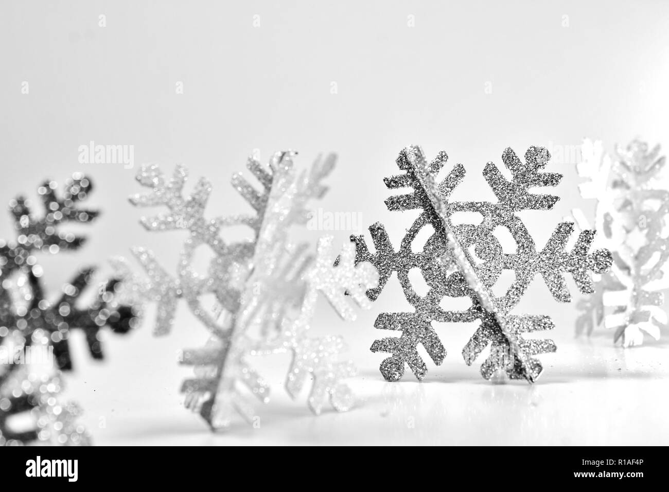 Glittery fiocchi di neve in una riga con un fiocco di neve in argento nel fuoco su sfondo bianco. Luminosa scena invernale Foto Stock