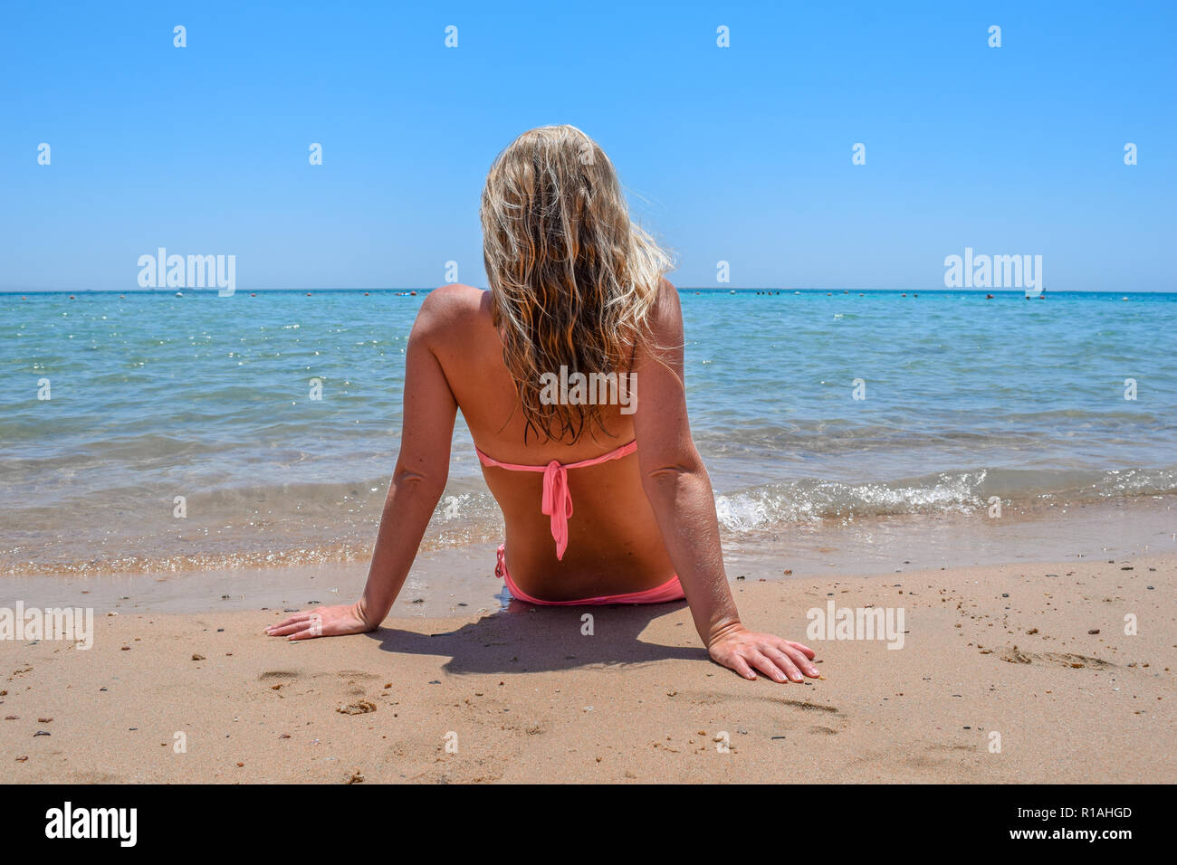 Donna seduta presso la spiaggia di sabbia di fronte all'oceano, bella donna di fronte oceano turchese Foto Stock