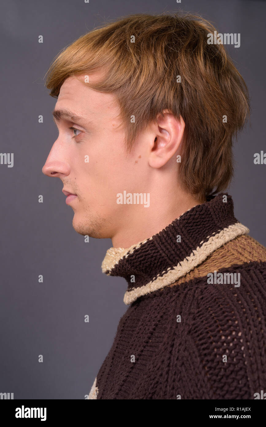 Giovane uomo bello con capelli biondi contro uno sfondo grigio Foto Stock